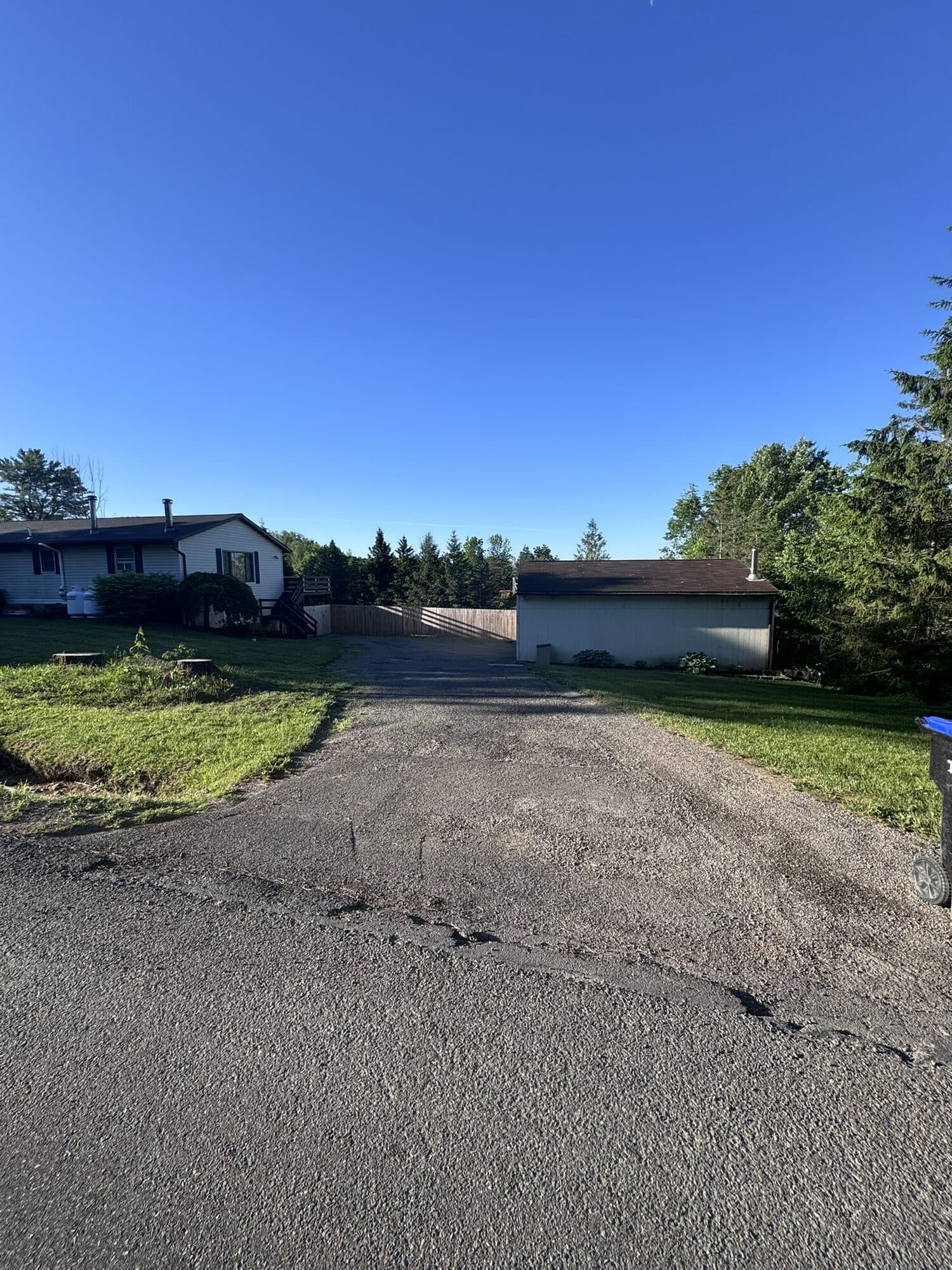 Smooth new stone and oil chip seal driveway curving toward a rural home under a clear blue sky.