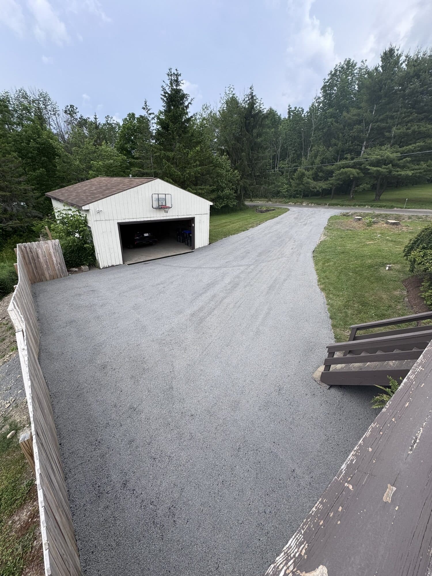 Freshly finished stone and oil driveway sloping to a garage beside a green lawn.