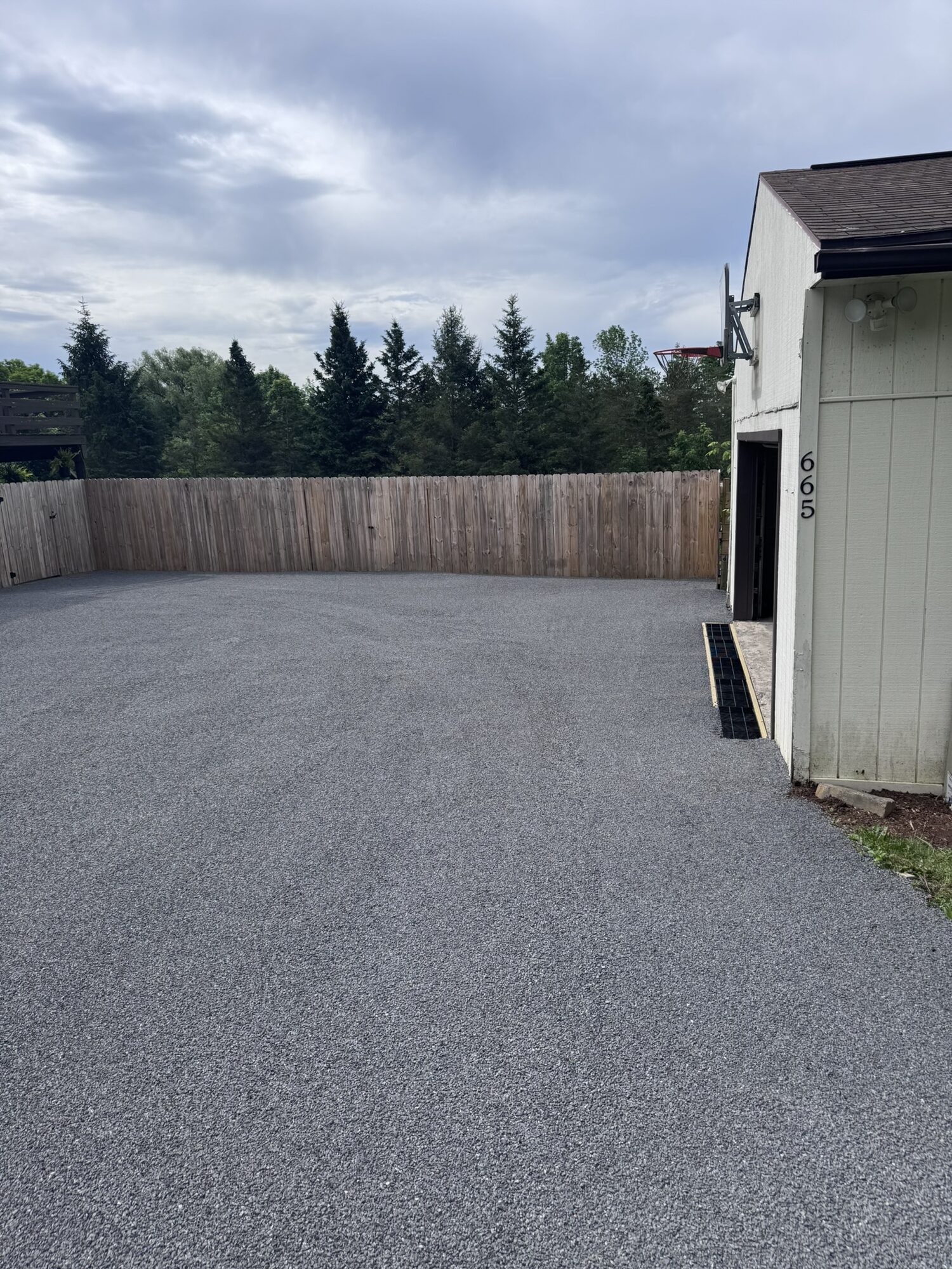 Smooth new chip seal driveway beside a white outbuilding after resurfacing.