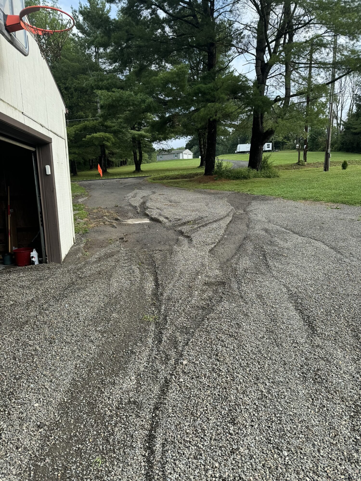 Cracked, rutted old gravel driveway in front of a rounded-roof garage before Rock Solid stone and oil resurfacing.