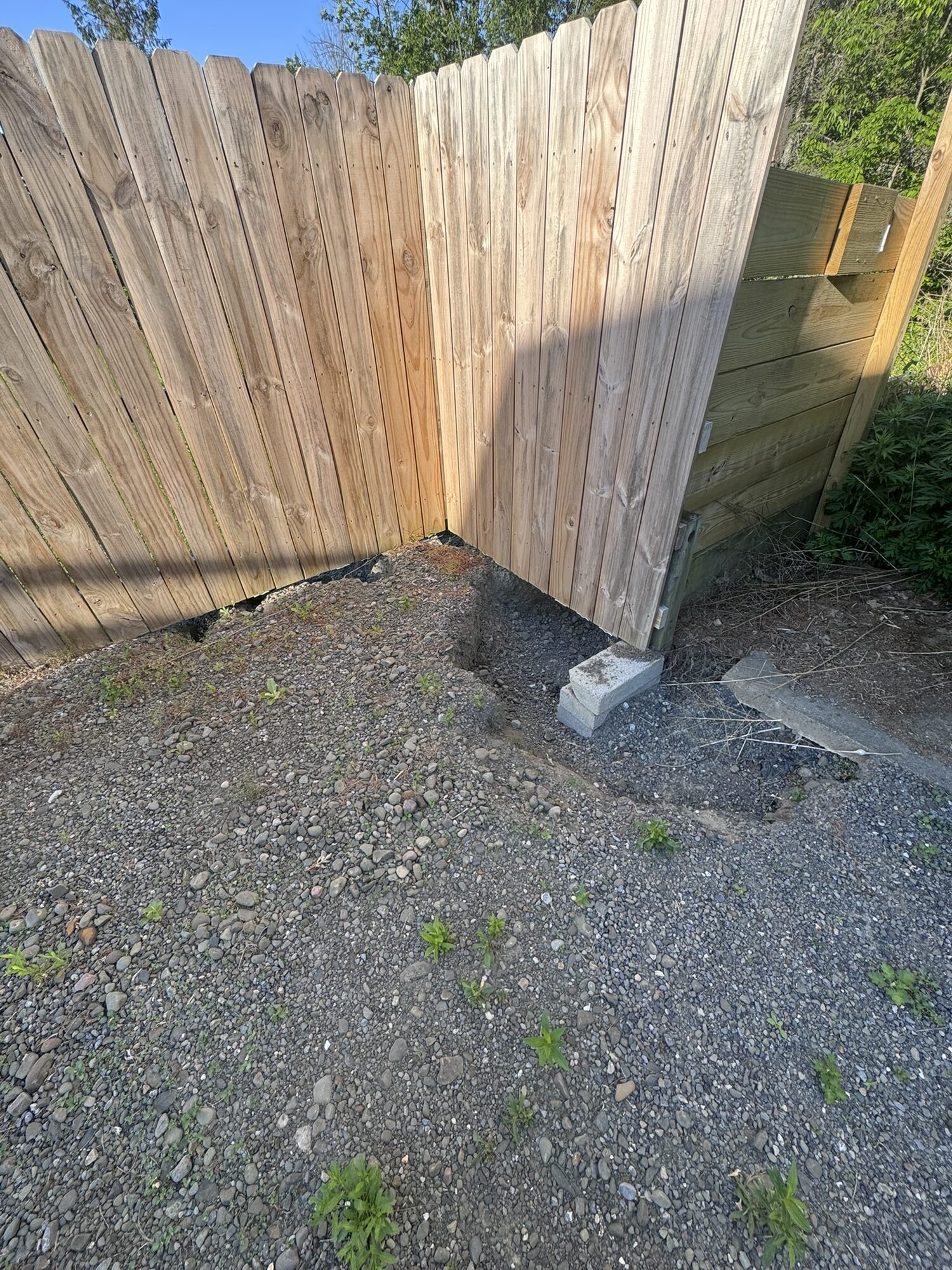 Weedy gravel in a fenced driveway corner before chip seal resurfacing.