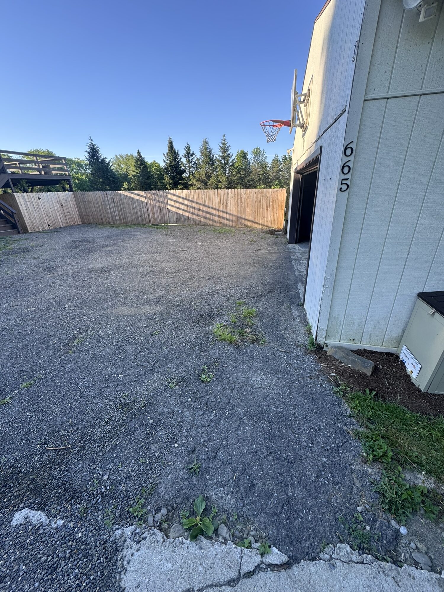 Worn, weedy gravel beside a white outbuilding before Rock Solid resurfacing.